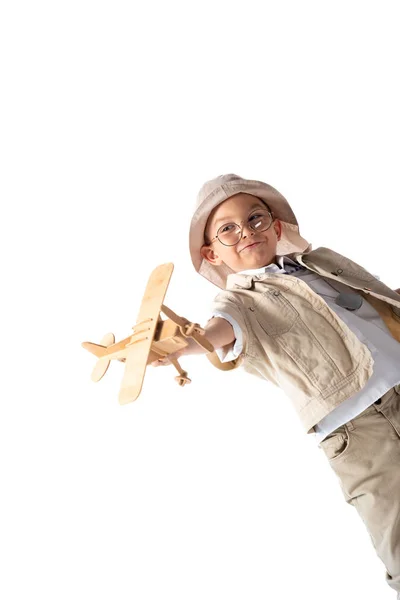 Sonriente explorador chico en gafas y sombrero celebración de juguete de madera plano aislado en blanco - foto de stock