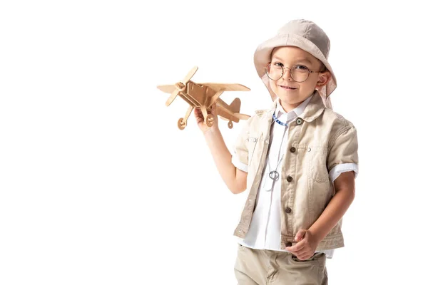 Lächelnder Entdeckerjunge mit Brille und Hut, Holzspielzeugflugzeug isoliert auf weißem Grund — Stockfoto