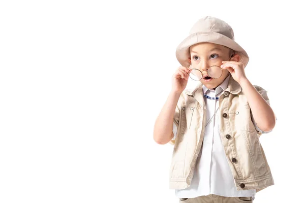 Niño explorador sorprendido en sombrero y gafas mirando hacia otro lado con la boca abierta aislada en blanco - foto de stock