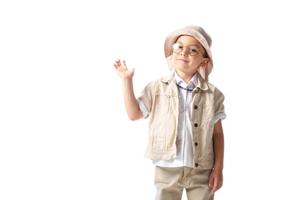 Menino explorador sorridente em chapéu e óculos olhando para a câmera e acenando mão isolada no branco — Fotografia de Stock