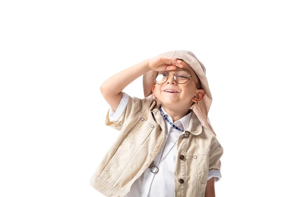 Niño explorador sonriente en gafas y sombrero mirando a distancia aislado en blanco - foto de stock