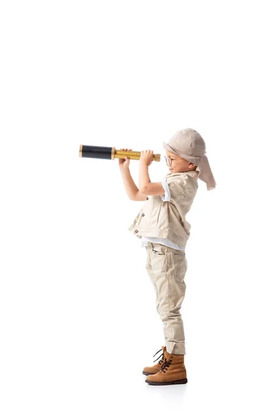 Full length view of explorer boy in glasses and hat looking through spyglass isolated on white — Stock Photo