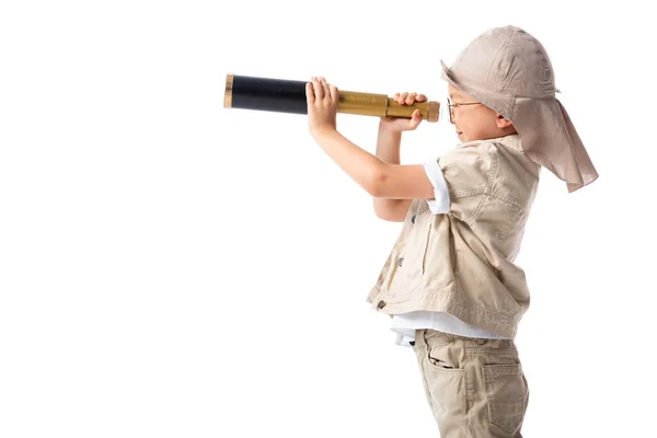 Side view of explorer boy in glasses and hat looking through spyglass isolated on white — Stock Photo