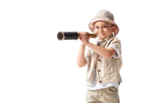 Curious smiling explorer boy in glasses and hat holding spyglass isolated on white — Stock Photo