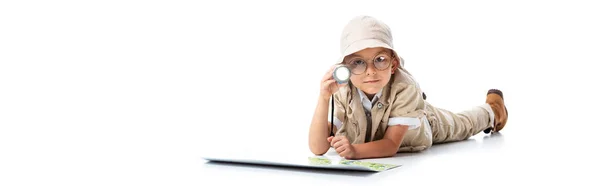 Panoramic shot of explorer boy in glasses holding flashlight and lying near map on white — Stock Photo