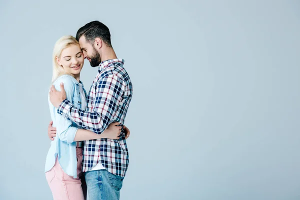 Guapo hombre abrazando hermosa sonriente joven mujer aislado en gris - foto de stock