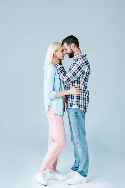 Hermosa pareja joven abrazándose y mirándose el uno al otro en gris - foto de stock