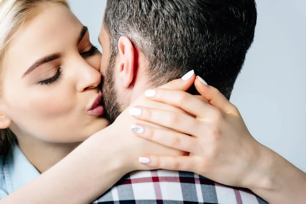 Linda menina loira beijando e abraçando o homem isolado no cinza — Fotografia de Stock