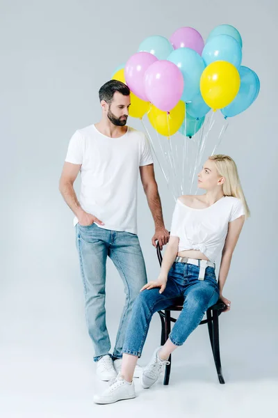 Mann und schönes Mädchen auf Stuhl in der Nähe von Luftballons auf grau — Stockfoto