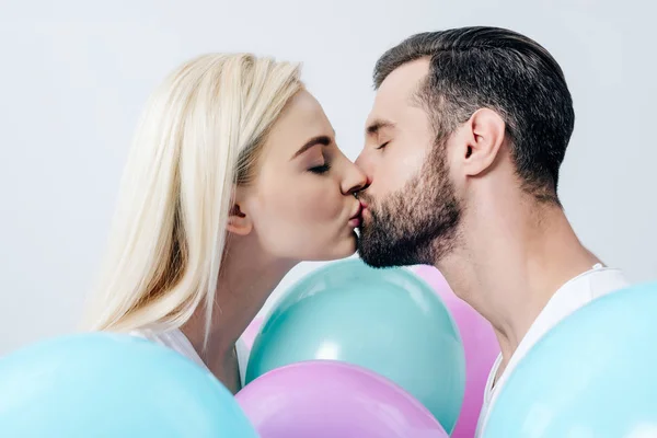 Hermosa pareja besándose cerca de globos aislados en blanco - foto de stock