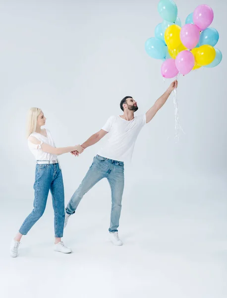 Schöne Mädchen hält Hand des Mannes mit Luftballons auf grau — Stockfoto