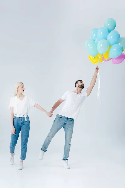 Schöne Mädchen hält Hand des Mannes mit Luftballons auf grau — Stockfoto