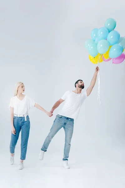 Bella ragazza che tiene la mano dell'uomo con palloncini su grigio — Foto stock