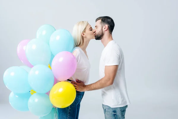 Чоловік і красива дівчина з повітряними кулями цілуються ізольовано на сірому — стокове фото