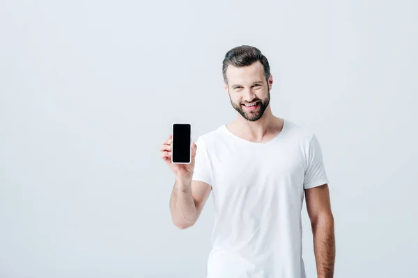 Щасливий чоловік показує смартфон з порожнім екраном ізольовано на сірому — стокове фото