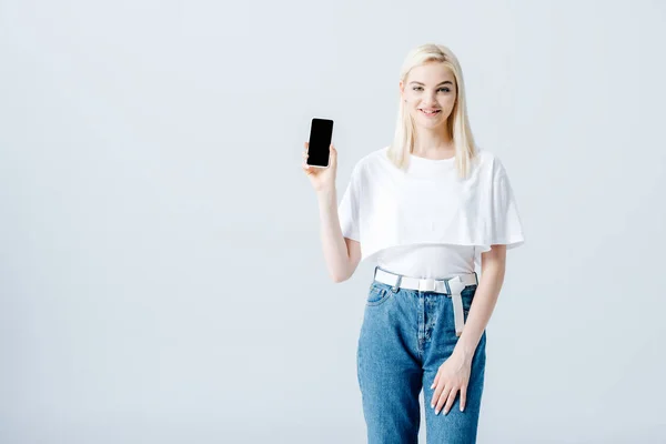 Красива щаслива блондинка, що показує смартфон з порожнім екраном ізольовано на сірому — стокове фото