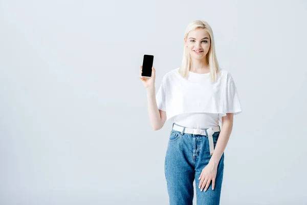 Bella ragazza bionda felice mostrando smartphone con schermo bianco isolato sul grigio — Foto stock