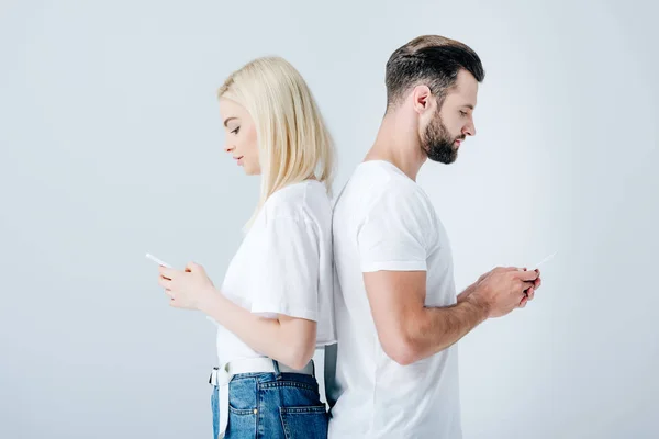 Man and beautiful girl standing back to back and using smartphones isolated on grey — Stock Photo