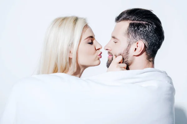 Beautiful girlfriend pouting lips near boyfriend covered in blanket on white — Stock Photo