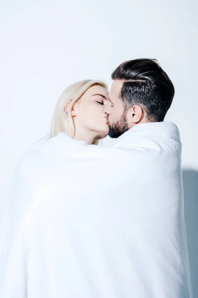 Belo casal com olhos fechados cobertos de cobertor beijando no branco — Fotografia de Stock