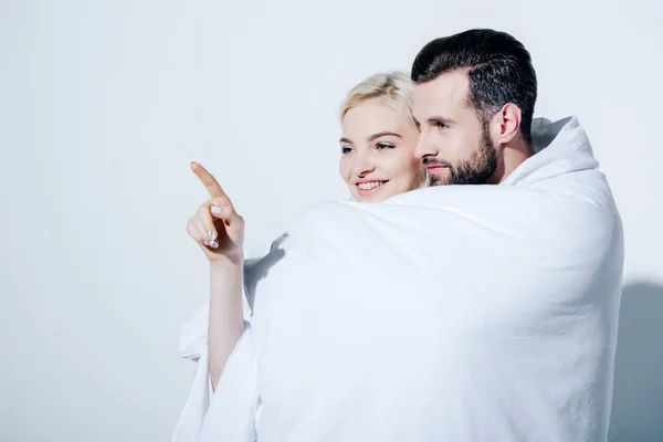 Petite amie pointant avec le doigt près du petit ami couvert de couverture sur blanc — Photo de stock