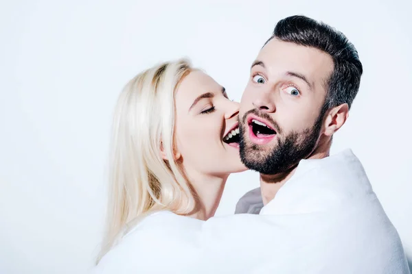 Girlfriend biting cheek of surprised boyfriend covered in blanket on white — Stock Photo