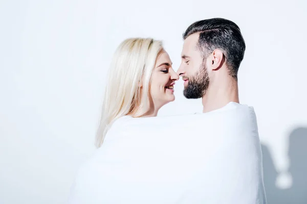 Smiling girlfriend and boyfriend covered in blanket on white — Stock Photo