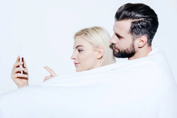 Man and beautiful girl covered in blanket using smartphone isolated on white — Stock Photo