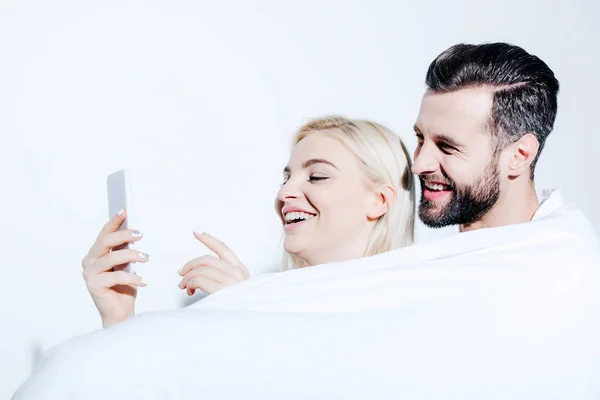 Man and beautiful girl covered in blanket using smartphone on white — Stock Photo