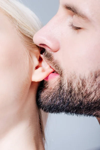 Close up of man biting ear of young woman isolated on grey — Stock Photo