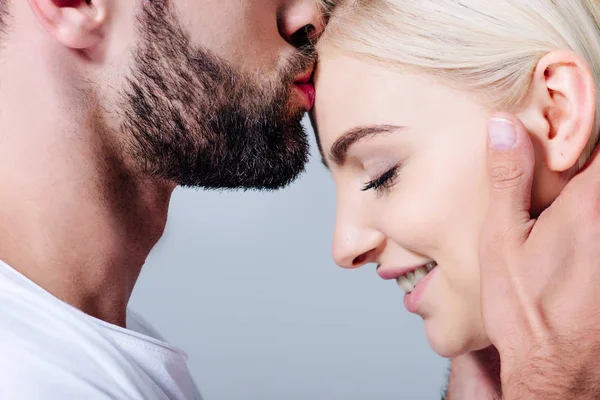 Мужчина целует в лоб красивую улыбающуюся девушку изолированную от серого — стоковое фото