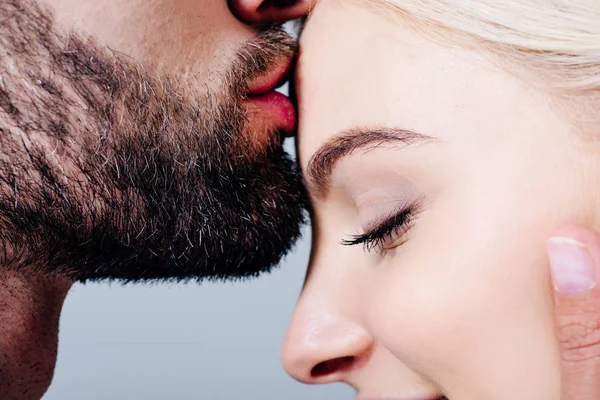 Mann küsst auf die Stirn schönes Mädchen isoliert auf grau — Stockfoto