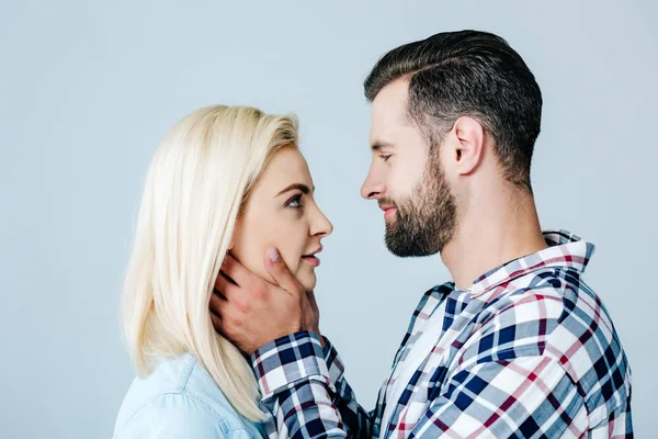 Handsome man embracing face of beautiful young woman isolated on grey — Stock Photo