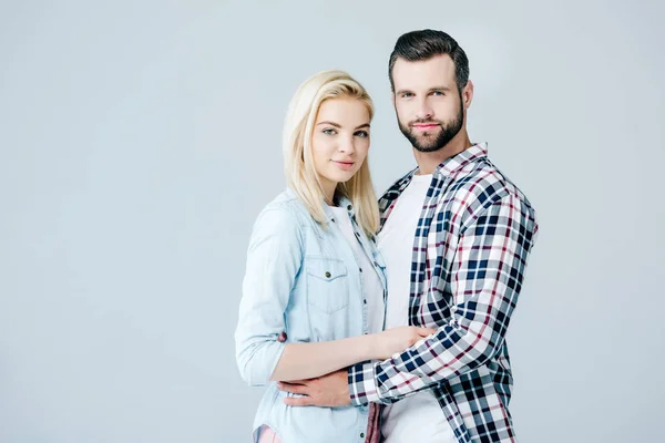 Schönes junges Paar, das sich umarmt und isoliert auf grau in die Kamera schaut — Stockfoto