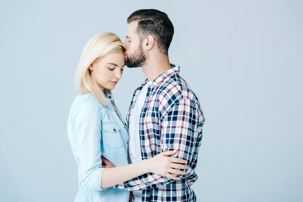Schöner Mann küsst schöne junge Frau isoliert auf grau — Stockfoto