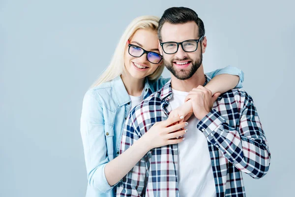 Schönes Mädchen mit Brille umarmt Mann isoliert auf grau — Stockfoto