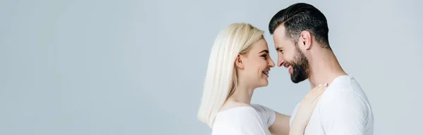 Панорамний знімок красивої усміхненої молодої пари, що обіймається ізольовано на сірому — стокове фото