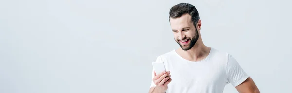 Панорамный снимок улыбающегося мужчины с помощью смартфона, изолированного на сером — стоковое фото