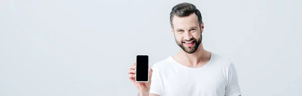 Панорамный снимок улыбающегося мужчины, показывающего смартфон с пустым экраном, изолированным на сером — стоковое фото