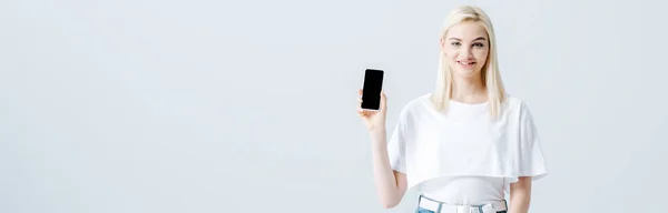 Tiro panorâmico de menina loira bonita mostrando smartphone com tela em branco isolado no cinza — Fotografia de Stock