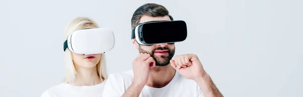 Plano panorámico de hombre con los puños cerrados y chica en auriculares de realidad virtual aislados en gris - foto de stock