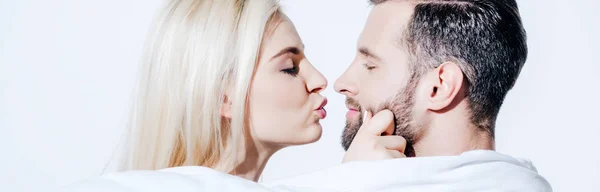 Panoramic shot of girlfriend pouting lips near boyfriend covered in blanket on white — Stock Photo