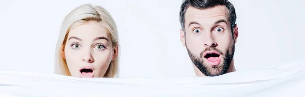 Panoramic shot of shocked girlfriend and handsome boyfriend holding blanket isolated on white — Stock Photo