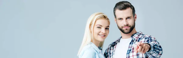 Panoramic shot of man pointing with finger near beautiful young woman isolated on grey — Stock Photo