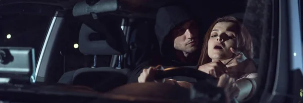 Панорамный снимок вора, душащего испуганную женщину в автомобиле ночью с ножом — стоковое фото