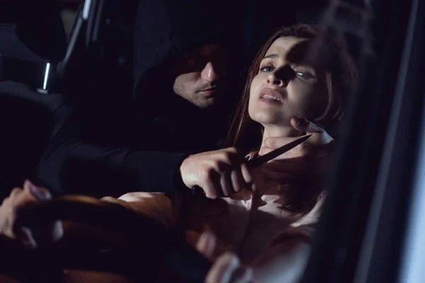 Thief strangling beautiful frightened woman in automobile at night with knife — Stock Photo