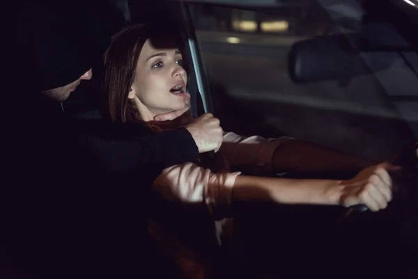Thief strangling beautiful frightened woman in automobile at night — Stock Photo