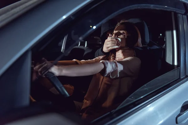 Ladrón cubriendo la boca de la mujer asustada en coche por la noche - foto de stock