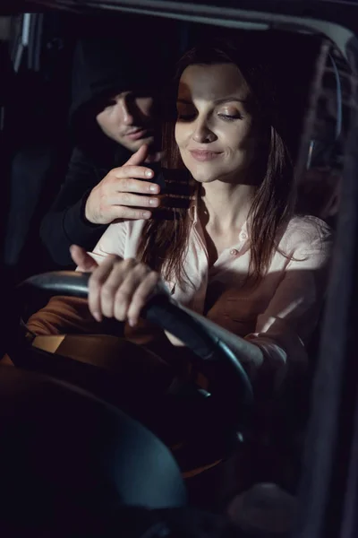 Ladrão escondido no banco de trás perto de bela mulher sorridente — Fotografia de Stock