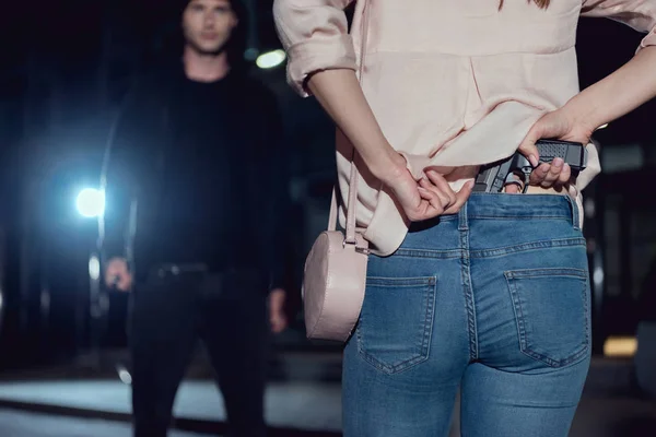 Вид ззаду жінка ховається пістолет за спиною біля злодія вночі — стокове фото
